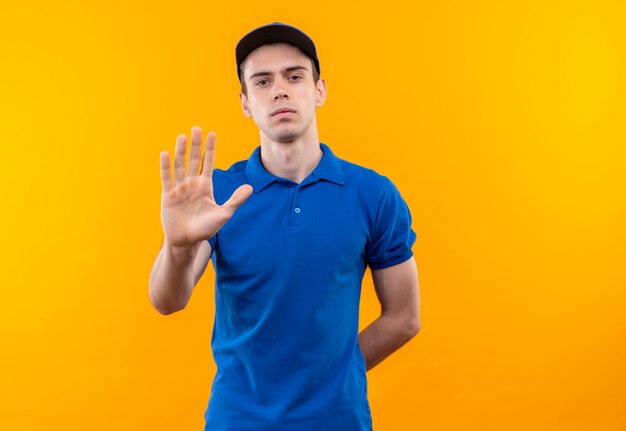 Jovem mensageiro vestindo uniforme azul e boné azul fazendo stop com a mão