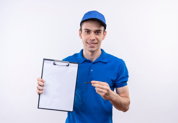 Jovem mensageiro vestindo uniforme azul e boné azul, sorrindo e apontando na prancheta com uma caneta