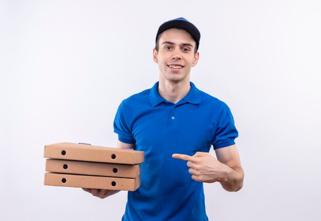 Jovem mensageiro vestindo uniforme azul e pontas azuis nas caixas de pizza com o dedo indicador