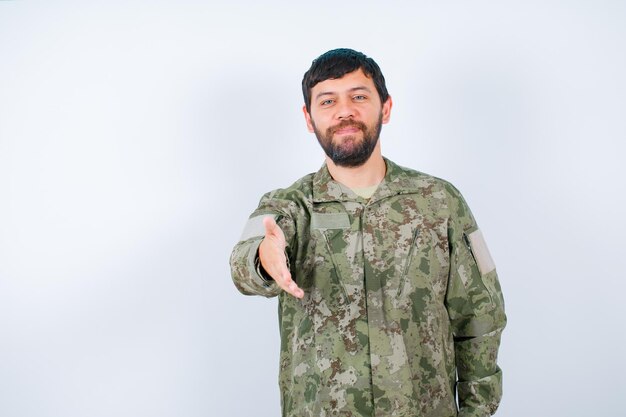 Jovem militar está mostrando oi gesto, estendendo a mão para a câmera no fundo branco