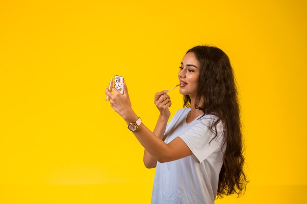 Jovem modelo aplicando brilho labial e olhando no espelho.