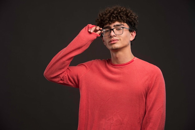 Jovem modelo com cabelos cacheados, tocando seus óculos.