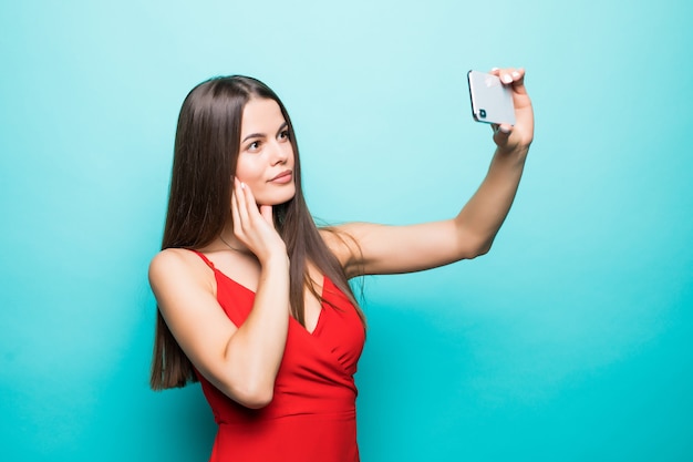 Jovem morena atraente alegre está sorrindo na parede azul. Ela está tirando uma selfie com o telefone, usando uma roupa casual de verão e um chapéu