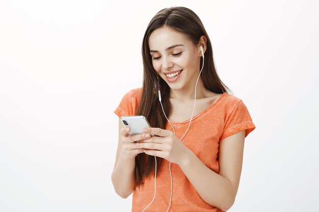 Jovem morena atraente ouvindo música em fones de ouvido e segurando o telefone celular