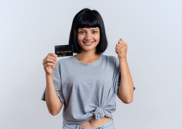 Jovem morena caucasiana sorridente segurando um cartão de crédito e segurando o punho