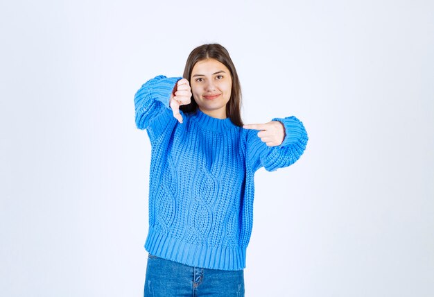 Jovem morena com suéter azul, apontando para algo em branco.