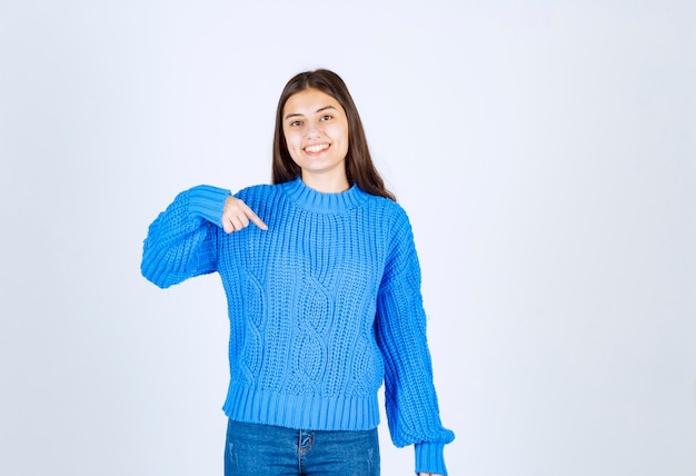 Jovem morena com suéter azul, apontando para algo em branco.