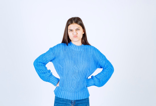 Jovem morena com suéter azul, olhando para a frente com expressão de raiva.