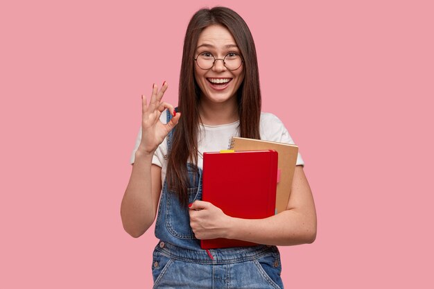 Jovem morena de macacão jeans segurando blocos de notas