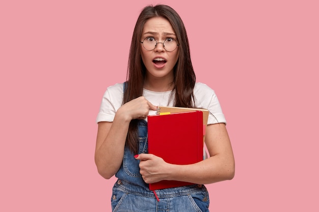 Jovem morena de macacão jeans segurando blocos de notas