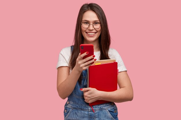 Jovem morena de macacão jeans segurando blocos de notas