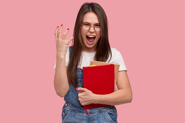 Jovem morena de macacão jeans segurando blocos de notas