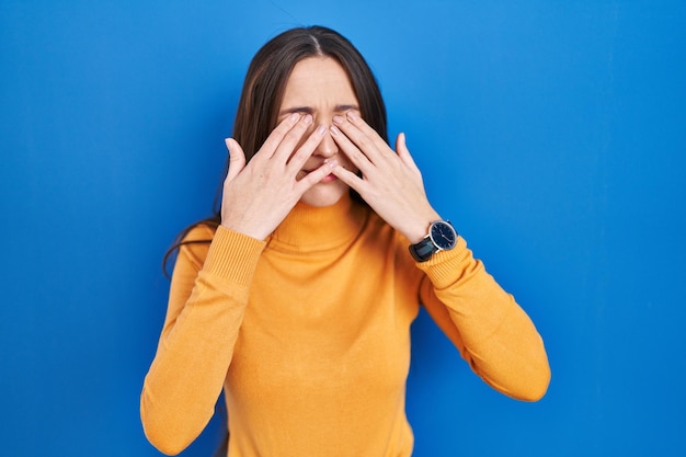 Foto grátis jovem morena em pé sobre fundo azul, esfregando os olhos para fadiga e dor de cabeça, problema de visão com sono e expressão cansada