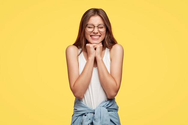 Jovem morena feliz com óculos posando contra a parede amarela