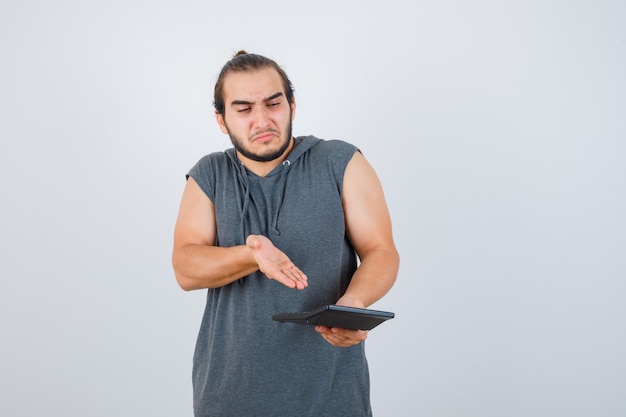 Jovem mostrando a calculadora com capuz e parecendo sombrio, vista frontal.