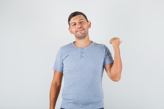 Jovem mostrando algo para trás em uma camiseta cinza e parecendo feliz