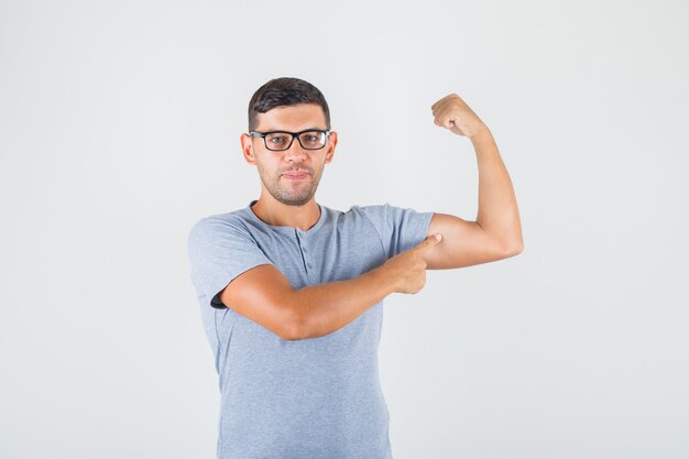 Jovem mostrando bíceps no braço em camiseta cinza, óculos