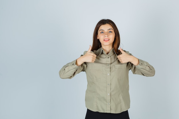 Jovem mostrando dois polegares para cima na camisa, saia e parecendo feliz. vista frontal.