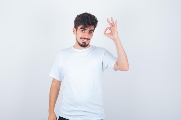 Jovem mostrando gesto de ok em camiseta branca e parecendo confiante