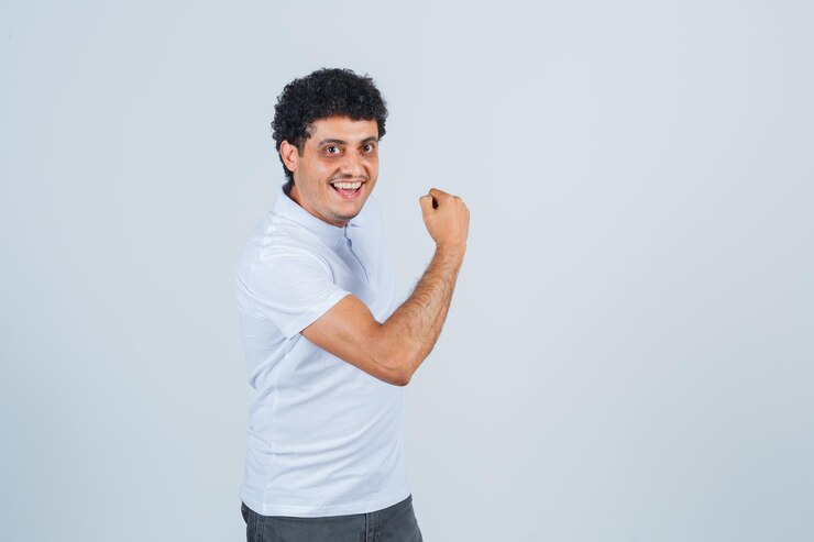 Foto grátis jovem mostrando gesto de poder em jeans e camiseta branca e parece feliz. vista frontal.