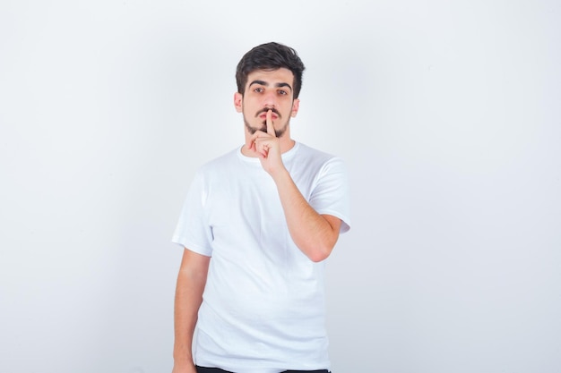 Jovem mostrando gesto de silêncio em uma camiseta branca e parecendo confiante