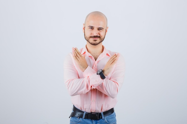 Jovem mostrando gesto fechado em camisa rosa, jeans, vista frontal.