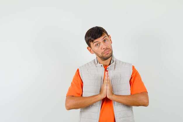 Jovem mostrando gesto namastê em camiseta, jaqueta e parecendo humilde.