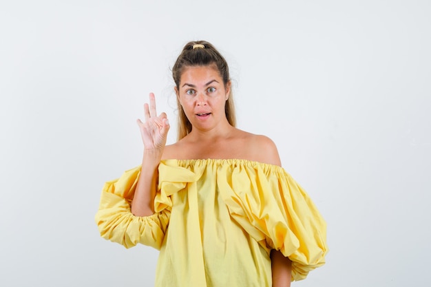 Foto grátis jovem, mostrando o gesto bem no vestido amarelo e olhando confiante, vista frontal.