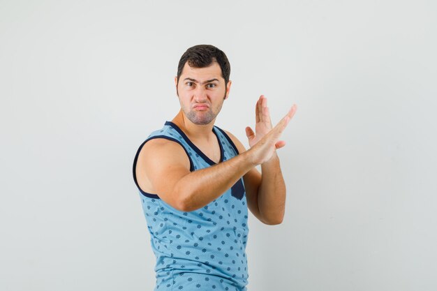 Jovem mostrando o gesto de golpe de caratê em camiseta azul e parecendo confiante. vista frontal.