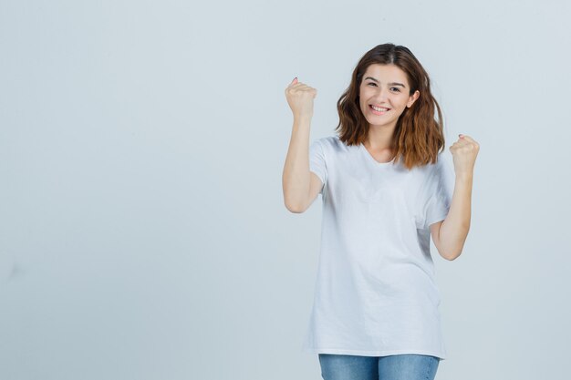 Jovem, mostrando o gesto do vencedor em t-shirt, jeans e parecendo com sorte, vista frontal.