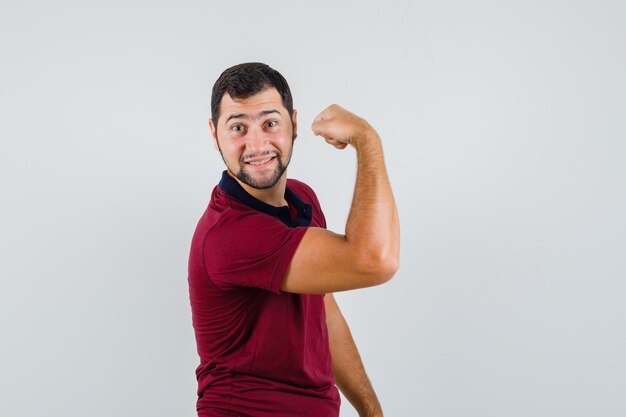 Jovem mostrando o músculo do braço em t-shirt vermelha e parecendo flexível, vista frontal.