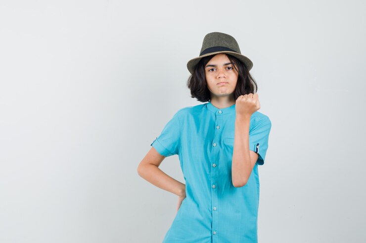Foto grátis jovem mostrando o poder do braço com camisa azul, chapéu e parecendo furiosa