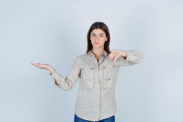 Jovem, mostrando o polegar para baixo gesto em casual, jeans e parecendo insatisfeito. vista frontal.