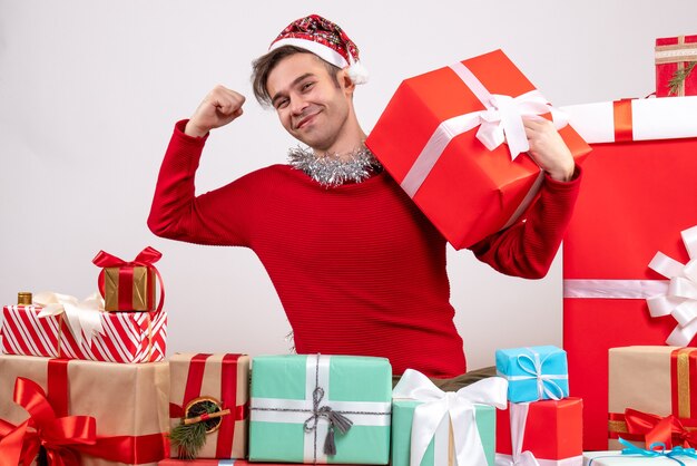 Jovem mostrando os músculos sentado em frente aos presentes de natal