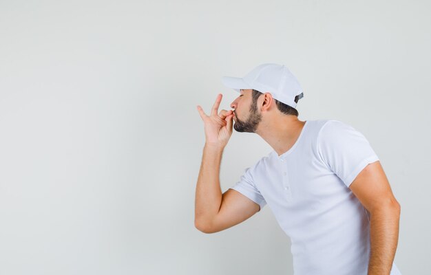 Jovem mostrando um delicioso gesto em t-shirt, boné e parecendo satisfeito.