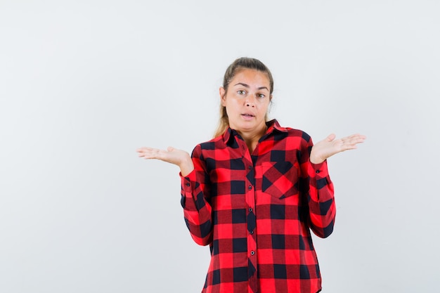 Jovem mostrando um gesto desamparado com uma camisa xadrez e parecendo confusa