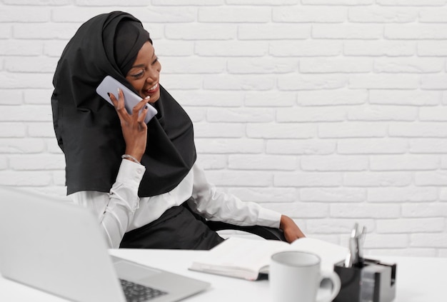 Jovem muçulmana de camisa e hijab falando por telefone