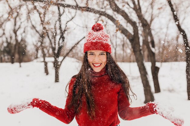 Jovem muito animada, cândida, sorridente, feliz, usando luvas vermelhas e chapéu, suéter de malha, andando brincando no parque na neve, roupas quentes, se divertindo