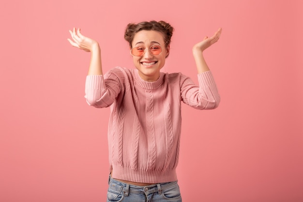 Jovem, muito animada, mulher rindo com carinha engraçada em um suéter rosa e óculos de sol na tendência de estilo primavera isolado no fundo rosa do estúdio