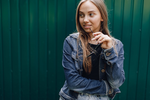 Jovem muito atraente em roupas jeans e óculos em um fundo verde escuro simples com um lugar vazio para o texto