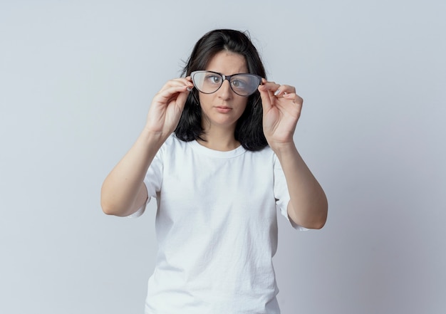 Jovem muito caucasiana segurando óculos e olhando para a câmera através deles, isolada no fundo branco com espaço de cópia