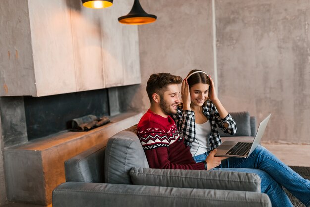 Jovem muito feliz e sorridente, homem e mulher sentados em casa no inverno, olhando no laptop, ouvindo fones de ouvido, alunos estudando online, casais em momentos de lazer juntos,