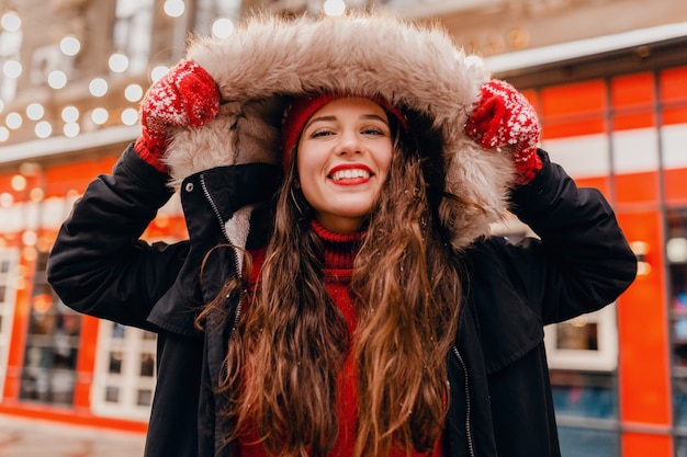 Foto grátis jovem, muito sorridente, feliz, com luvas vermelhas e chapéu de malha, vestindo um casaco de inverno, andando na rua da cidade, roupas quentes