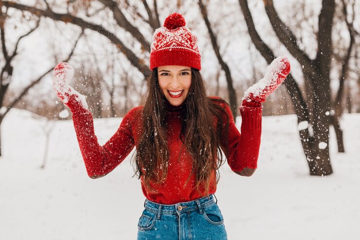 Foto grátis jovem, muito sorridente, feliz, com luvas vermelhas e chapéu, suéter de malha, caminhando no parque na neve, roupas quentes, se divertindo
