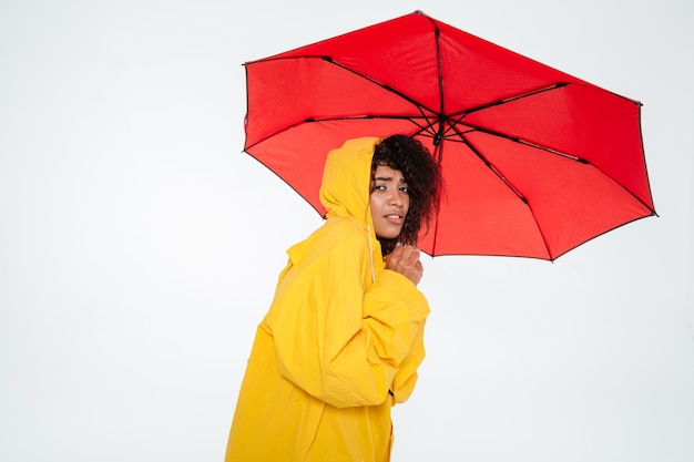 Jovem mulher africana na capa de chuva se escondendo atrás do guarda-chuva