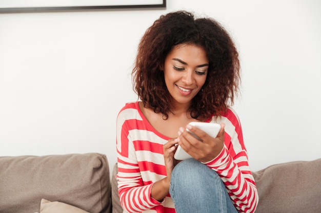 Jovem mulher africana no sofá conversando no smartphone