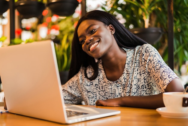 Jovem mulher africana sentada em um café, trabalhando em um laptop