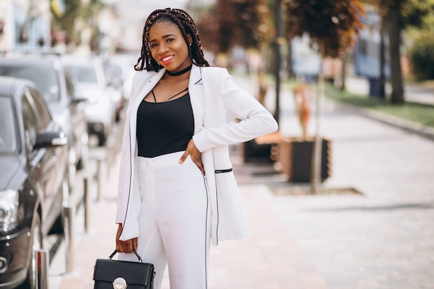 Jovem mulher africana vestida de terno branco do lado de fora da rua