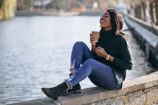 Jovem mulher afro-americana a beber café à beira do lago