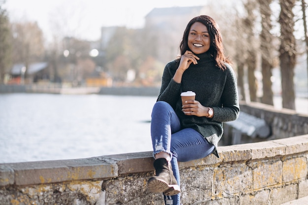 Jovem mulher afro-americana a beber café à beira do lago